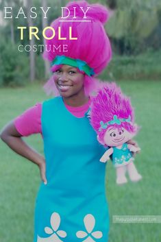 a woman with pink hair and blue dress holding a troll doll in front of her