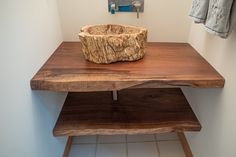 a wooden bowl sitting on top of a wooden table in a white walled room next to a coat rack