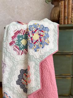 a quilted blanket sitting on top of a dresser next to a book case and vase