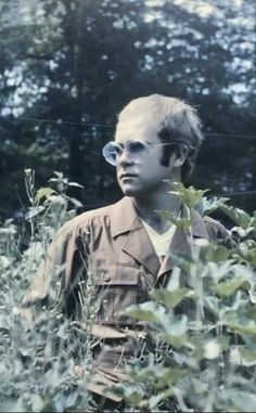 an old photo of a man standing in the middle of tall grass with trees behind him