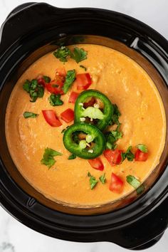 a crock pot filled with soup and garnished with bell peppers, cilantro and green peppers