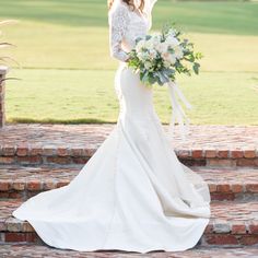 a woman in a wedding dress is standing on some steps and holding a flower bouquet