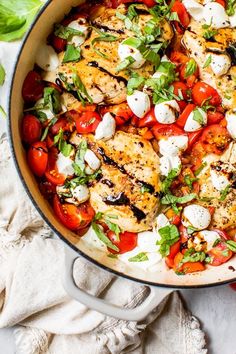 a skillet filled with chicken, tomatoes and mozzarella on top of a table