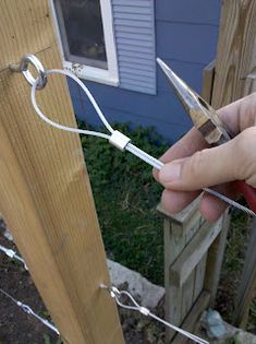 someone is holding scissors in their hand near a fence and house with a blue door