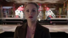 a woman with short hair wearing a brown blazer and red lipstick in a room full of stained glass windows