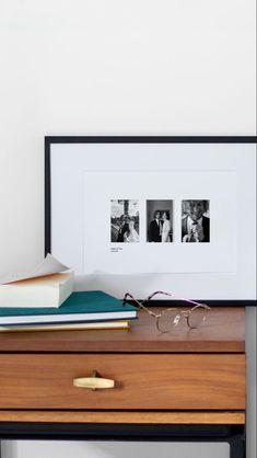 a wooden desk topped with books and glasses next to a framed photo on top of it