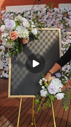 a woman standing in front of a sign with flowers on it and holding a flower arrangement