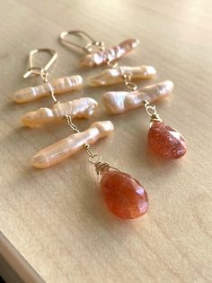 "These earrings remind me of summer! Still a little far off, given the fact that it's only February, but they have a warm vibe all the same. These are peach-toned freshwater biwa stick pearls, center-drilled and wire-wrapped with 14K gold-filled wire above juicy 14mm faceted sunstone pear briolettes. 3\" long, from bottom of briolettes to top of the gold-filled kidney ear wires. Your jewelry will arrive gift-boxed, and gift-wrapping is available upon request. Thanks for checking out my shop!" Keshi Pearl Jewelry, Pearl Earrings Designs, Pebble Jewelry, Peach Jewelry, Pearl Jewelry Design, Biwa Pearls, Silver Earrings Handmade, Peach Fuzz, Pearl Necklaces