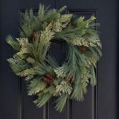 a wreath is hanging on the front door with pine cones and evergreen needles in it