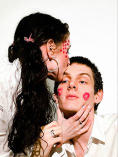 two people with their faces painted red and white, one is kissing the other's cheek