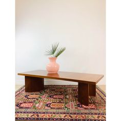 a pink vase sitting on top of a wooden table next to a colorful area rug