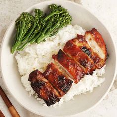 a white plate topped with meat and rice next to broccoli on top of a table