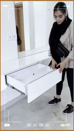 a woman standing in front of a mirror holding an open drawer with the lid closed