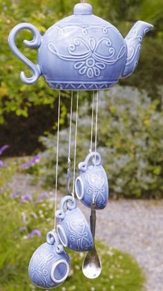 a blue teapot wind chime is hanging from a tree in front of some purple flowers