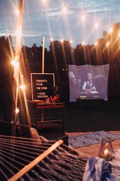 a hammock in the middle of a yard with lights on it and a movie screen