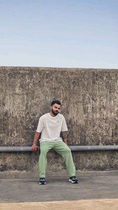 a man sitting on top of a cement wall next to a skateboarder in white shirt and green pants