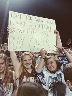 two girls holding up a sign in the middle of a crowd at a football game