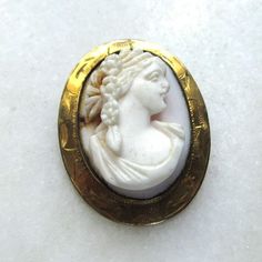 "This is a vintage gold-filled cameo brooch.  The cameo is carved from very pale pink/white shell.  The bezel has etched design around the lip.  The pin back is secure.  The brooch measures 1 1/4\" long x 1\" wide.   This is a vintage, previously owned brooch. Therefore, light wear can be expected.  There is no visible damage." White Cameo Brooch For Formal Occasions, White Cameo Brooches For Formal Occasion, White Cameo Brooches For Wedding, White Cameo Brooch For Wedding, White Cameo Wedding Brooches, White Victorian Cabochon Brooches, Victorian White Cabochon Brooches, Victorian Style White Cameo Brooches, Victorian Style White Cameo Brooch