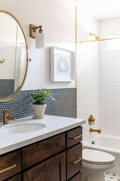 a bathroom with blue and white tiles on the walls, a round mirror over the bathtub, and a potted plant