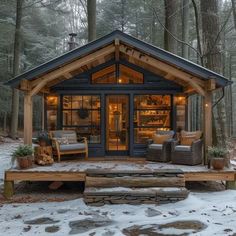 a small cabin in the woods with snow on the ground and two chairs sitting outside