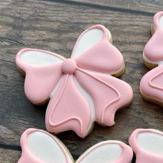 four decorated cookies with pink icing and bows on them sitting on a wooden table