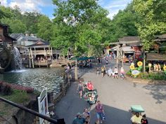 people are walking down the street in front of shops and water features at an amusement park