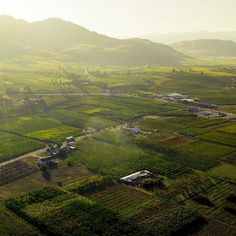 an aerial view of a farm land with houses and trees in the distance, surrounded by mountains