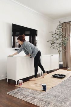 a woman standing on top of a white cabinet in front of a flat screen tv