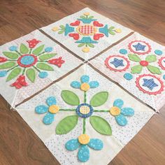 four quilted squares with flowers on them sitting on a wooden floor in front of a wood floor