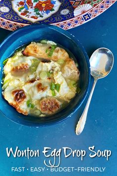 an egg drop soup is in a blue bowl with spoons next to it on a blue table