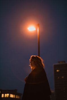 a woman standing under a street light at night with her hair blowing in the wind