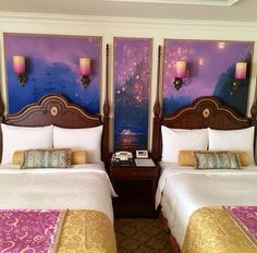 two beds in a hotel room with paintings on the wall and lamps hanging above them