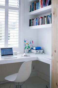 a laptop computer sitting on top of a white desk next to a book shelf filled with books