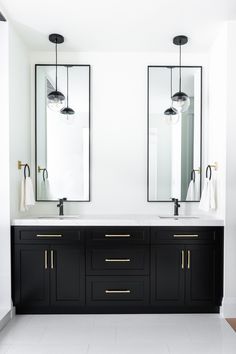 two black and white sinks in a bathroom with mirrors on the wall above them, along with hanging lights