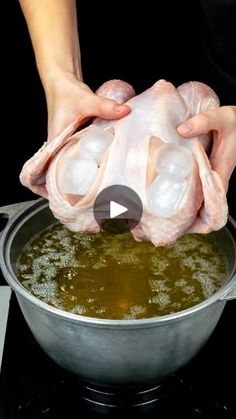 a person is holding raw chicken in a pot on the stove with green liquid being poured into it