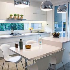 a kitchen with white chairs and an island in front of the counter top that has plants on it