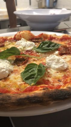 a close up of a pizza on a plate with cheese and spinach toppings