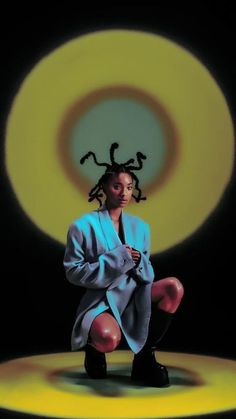 a woman with dreadlocks sitting in front of a yellow and black circular background