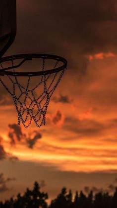 a basketball hoop with chains hanging from it in front of an orange and black sky