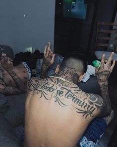 a man with tattoos on his back sitting on a couch next to two other men