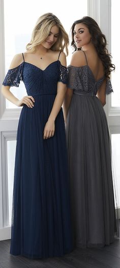 two women in dresses standing next to each other looking at the same person's reflection