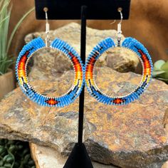 These striking hoop earrings are a vibrant showcase of beadwork, blending traditional craftsmanship with a contemporary design. The hoops are wrapped in a colorful array of beads, featuring a gradient of blue, red, yellow, black, and white. The bold colors are reminiscent of the natural beauty of the Southwestern landscape, with a pattern that mimics the radiant colors of a sunset. The intricate beadwork is evenly spaced, creating a balanced and symmetrical look that is eye-catching and artistic Hoop Beaded Earrings, Southwestern Landscape, Red Hoop Earrings, Native American Beadwork Patterns, Native American Earrings, Native American Beadwork, Beadwork Patterns, Fringe Earrings, Native American Jewelry