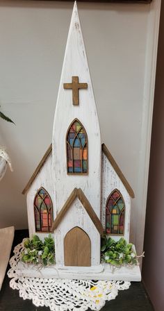 a small white church with stained glass windows on the front and side walls is sitting on a lace doily