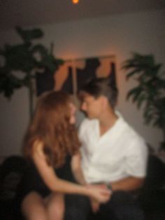 a man and woman sitting next to each other in a room with plants on the wall