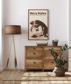 a poster hangs on the wall next to a wooden dresser and potted plant in front of it