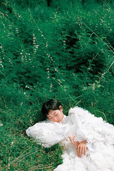 a woman in a white dress laying on the ground surrounded by tall grass and flowers