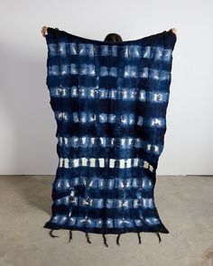 a person holding up a blue and white tie dyed blanket in front of a wall