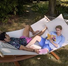 two people laying in a hammock reading books