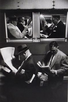 black and white photograph of two men sitting on a subway car reading newspapers while another man looks out the window