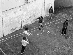 several people are playing soccer in an alleyway with graffiti on the wall and one person is throwing a ball